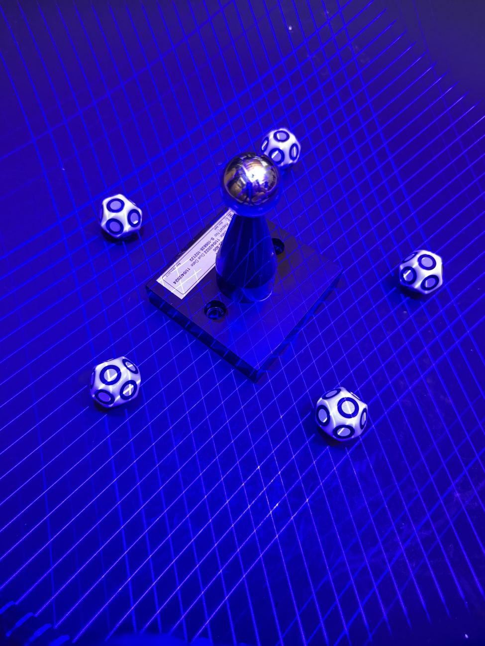 PoseMark dice on a plate under a scanner's blue laser grid, beside a calibration sphere, mid-scan